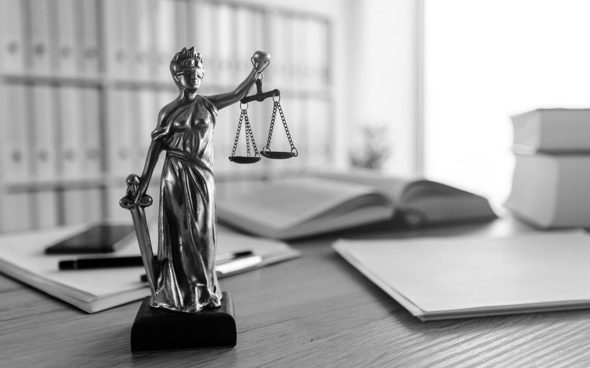 A black and white photo of a statue of justice holding scales of justice on a desk.