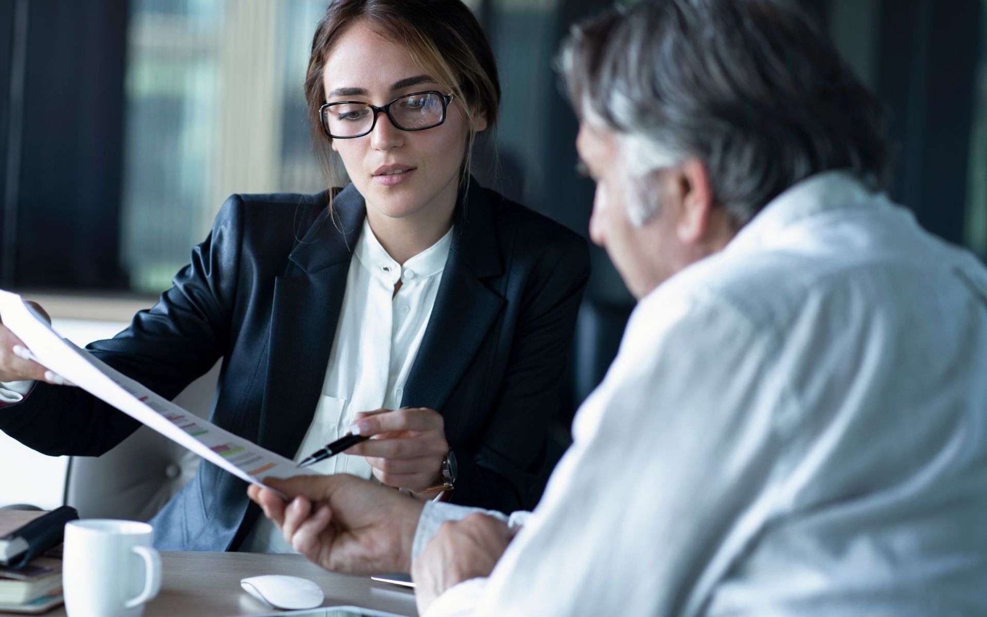A woman is sitting at a table talking to a man while holding a piece of paper.