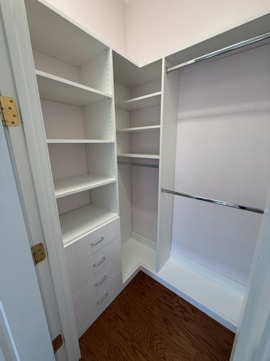 White walk-in closet with shelves, drawers, and hanging rods. Brown hardwood floor and pink walls.