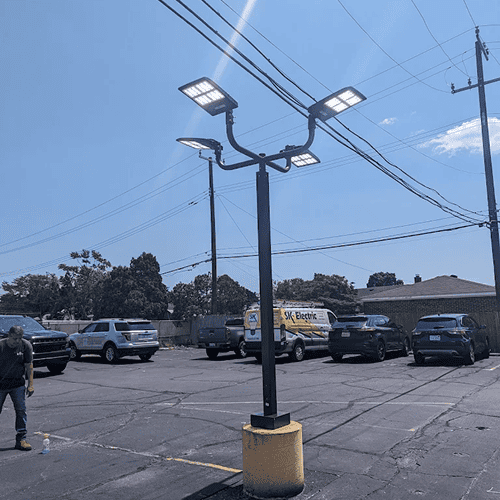 Parking lot with a tall solar light pole and parked cars under a clear blue sky.