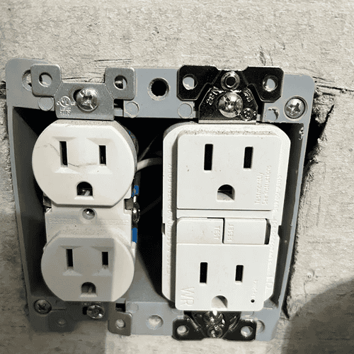 Two duplex electrical outlets in a wall, one white and one cream, with exposed mounting brackets.