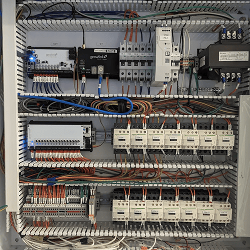 Electrical control cabinet with neatly wired relays, breakers, and terminal blocks on metal shelves