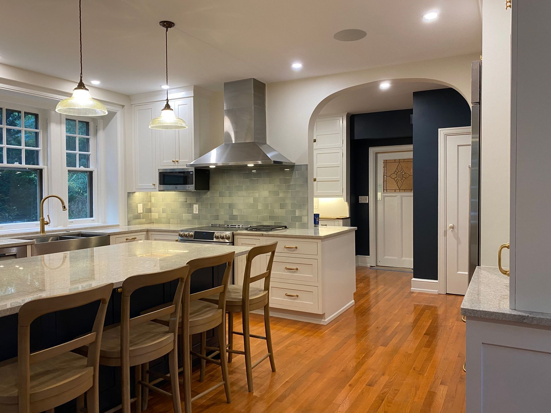 A kitchen with wooden floors , white cabinets , stainless steel appliances and a large island. James McCoy Remodeling Services Serving 19072,19003,19118,19444,19095 and surrounding areas