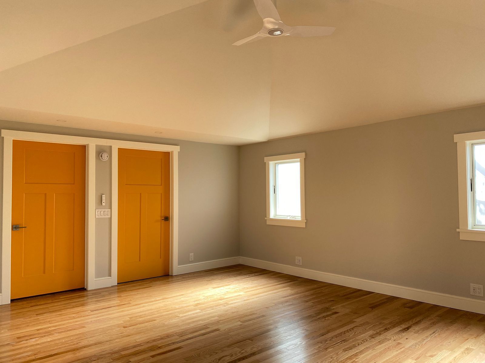 An empty room with two yellow doors and a ceiling fan.