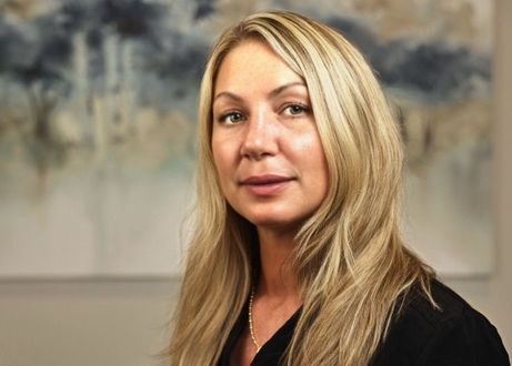 Portrait of Nicole Smith, dental hygienist for Dr. Donald Marks, in a black top against an abstract painting background