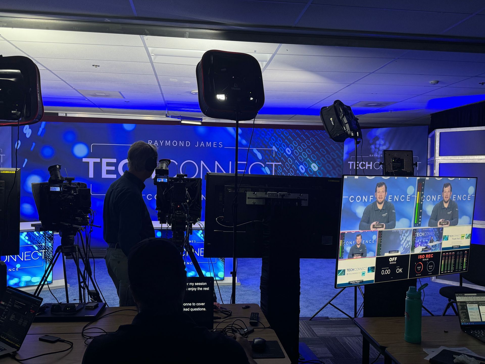 A technical crew operates cameras and monitoring equipment in a production studio with a large