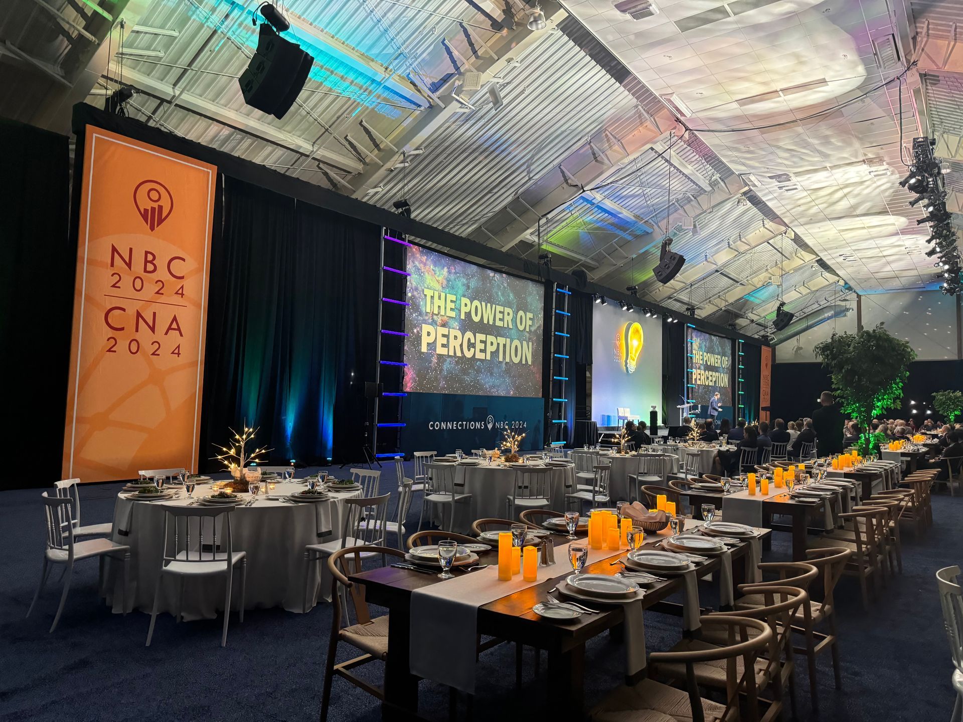 A conference hall set for a gala dinner, featuring round tables, warm candlelight, and