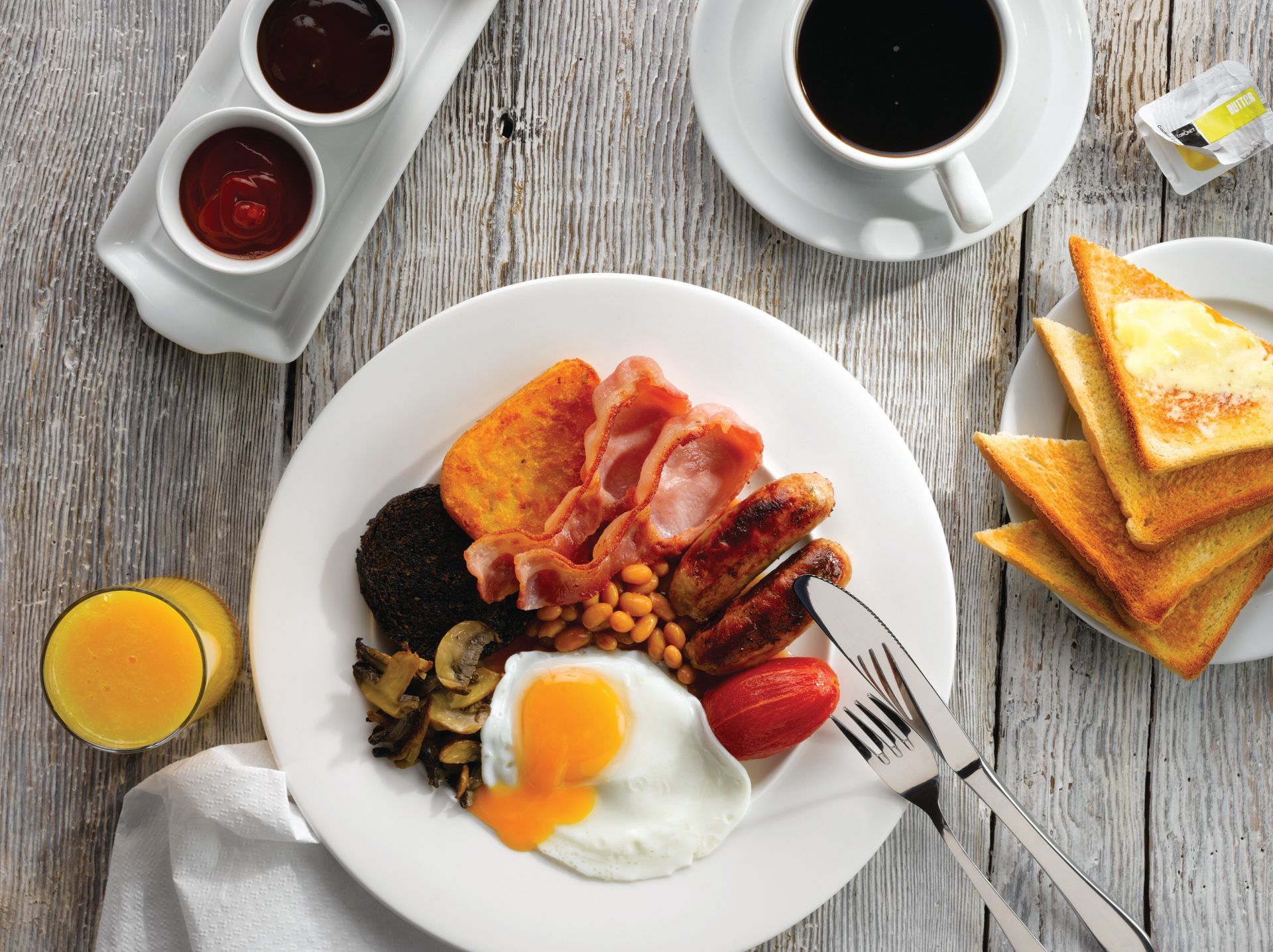 Breakfast spread with eggs, bacon, toast, fruit, and coffee on a rustic table