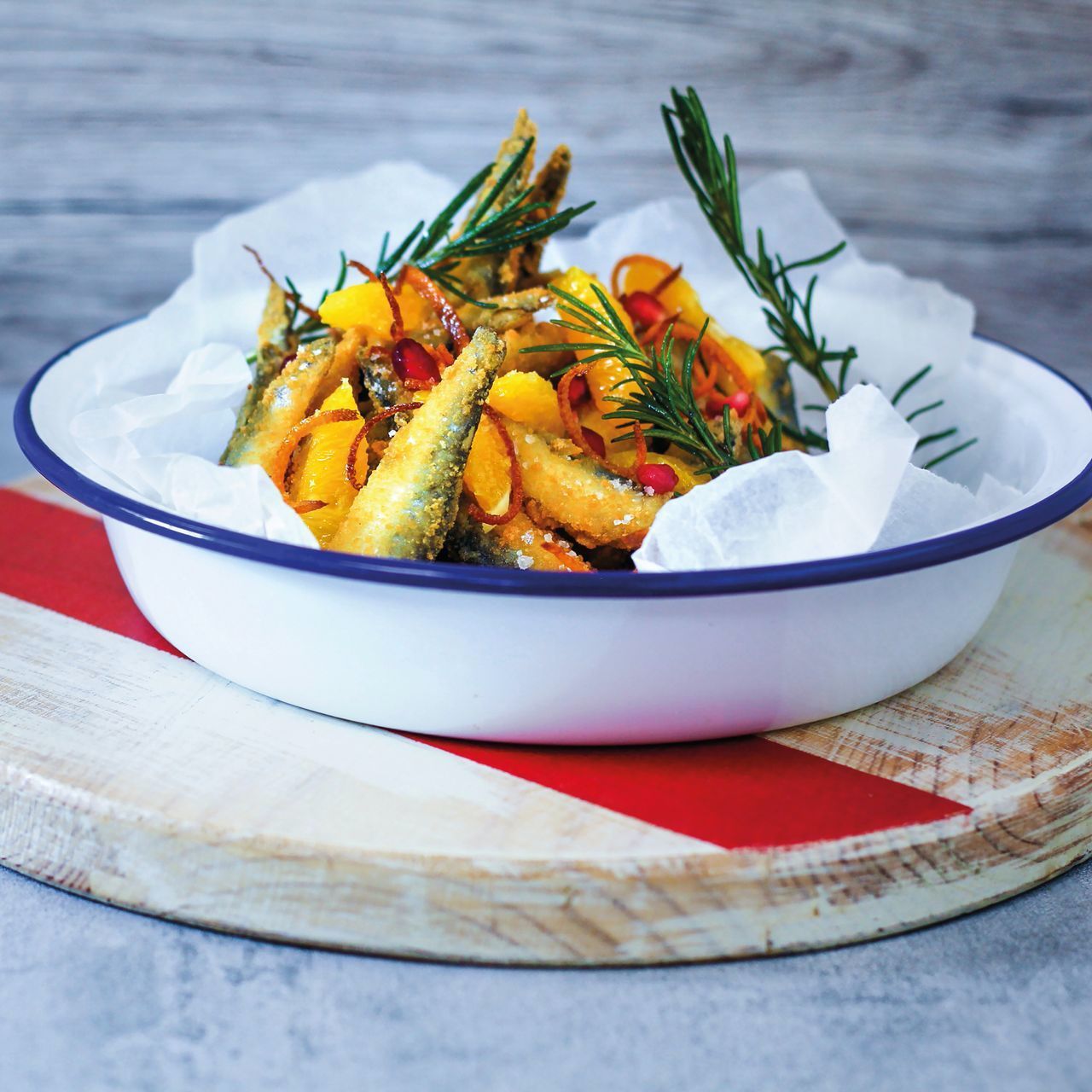 Roasted vegetables with rosemary served in a white bowl on a wooden board