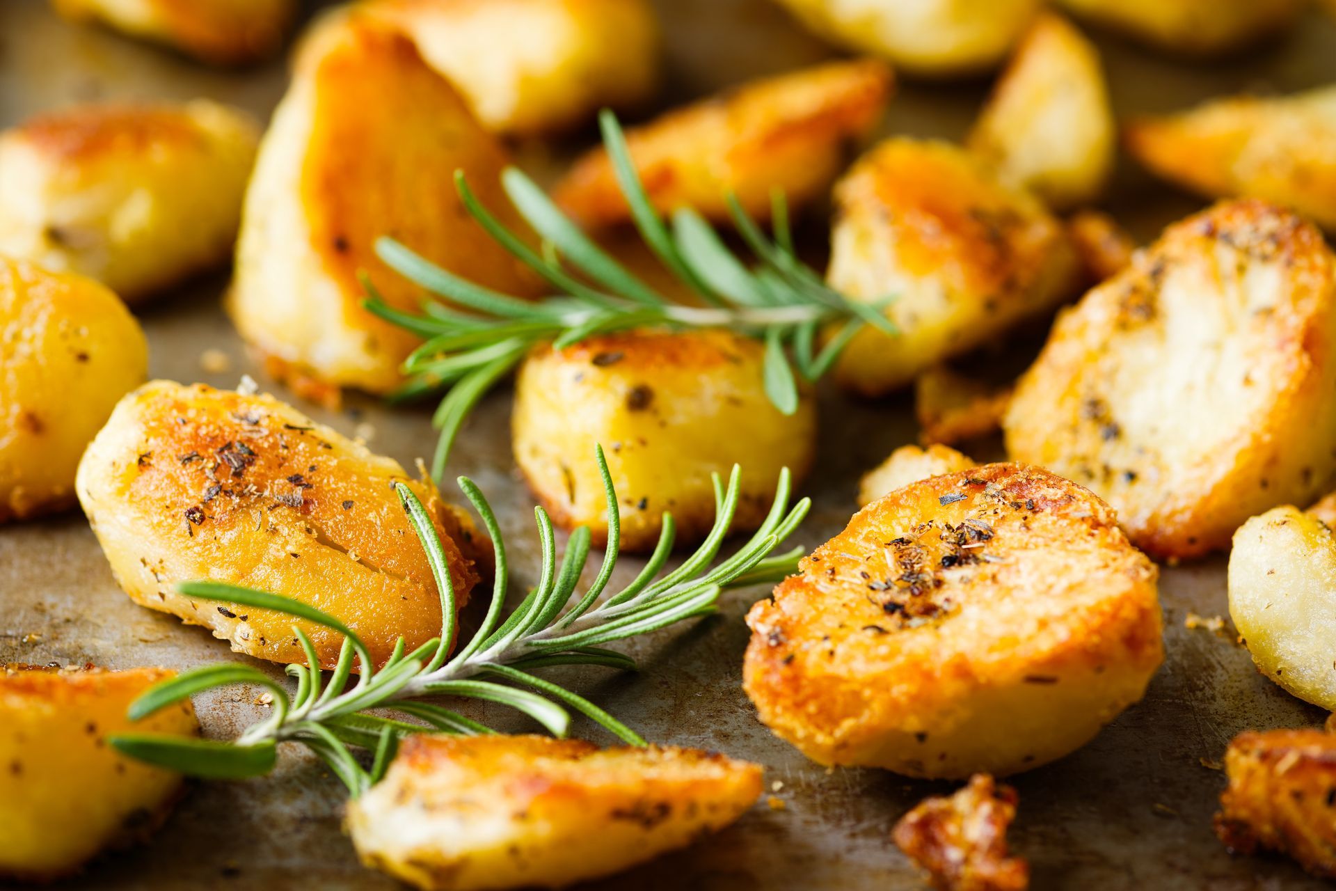 Roasted potato wedges with rosemary on a baking tray, golden and crisp