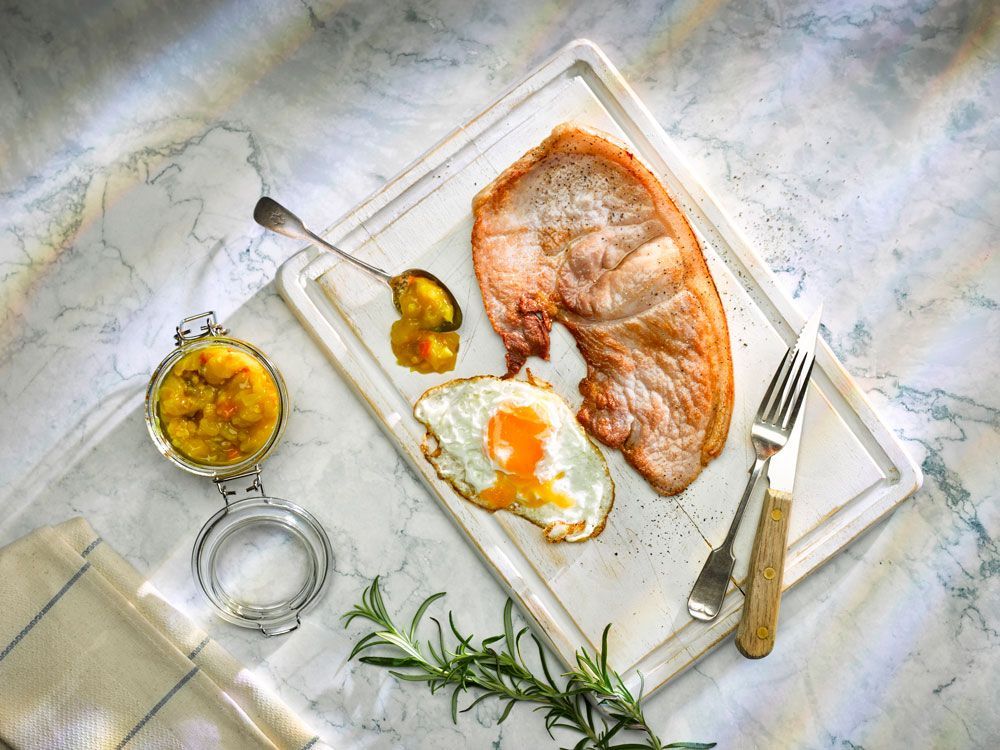 Roasted fish fillet on a white board with lemon, herbs, and small bowls of sauce on a marble surface