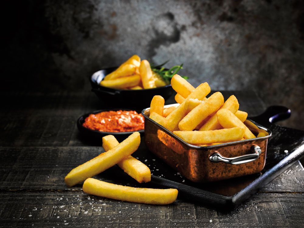 French fries in a wooden serving tray with dipping sauces on a dark table.