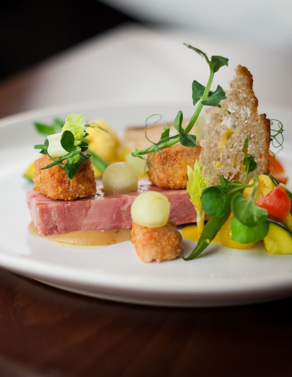 Gourmet plated dish with vegetables, herbs, and crispy garnish on a white plate