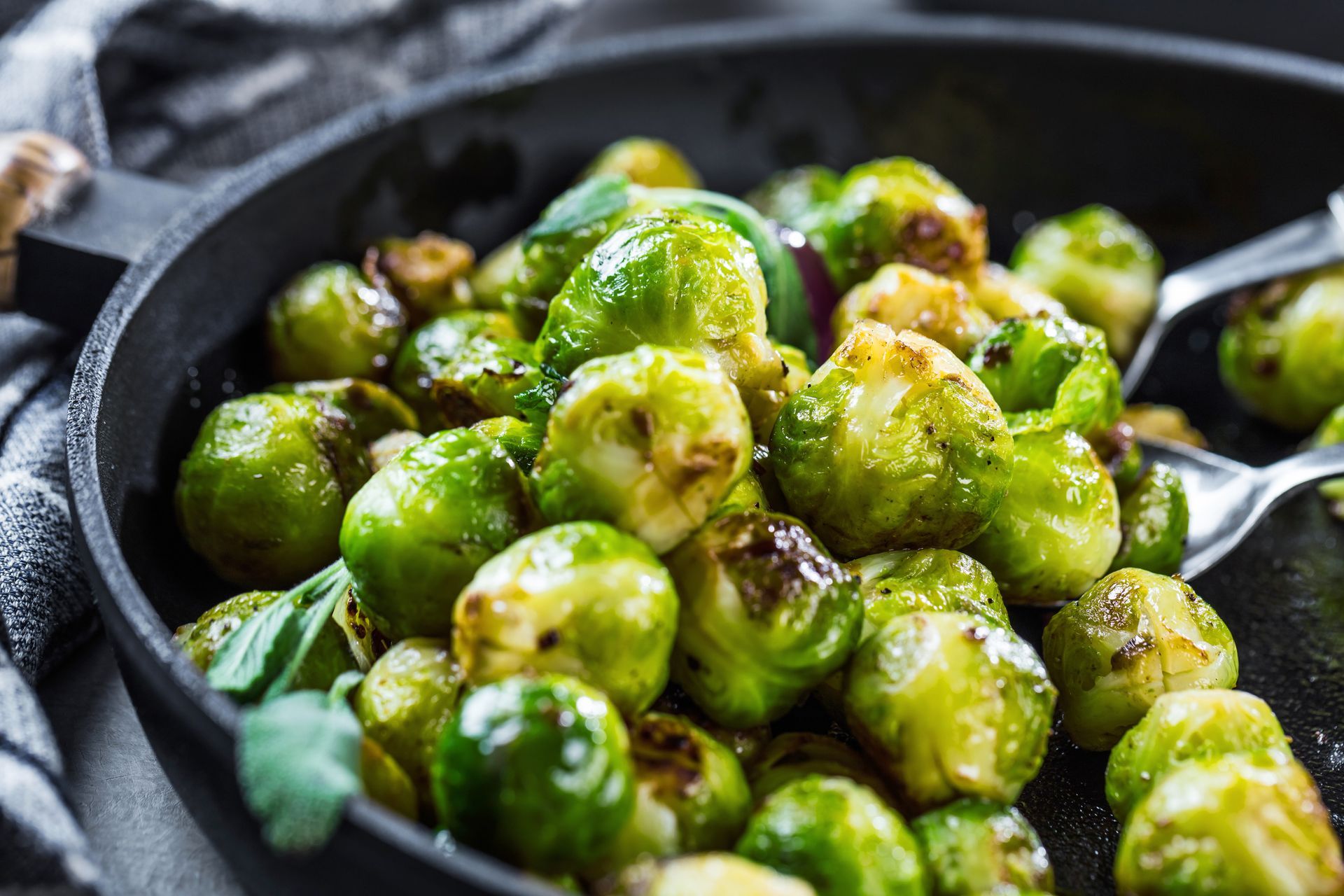 Pan of roasted Brussels sprouts with a spoon, glistening with seasoning
