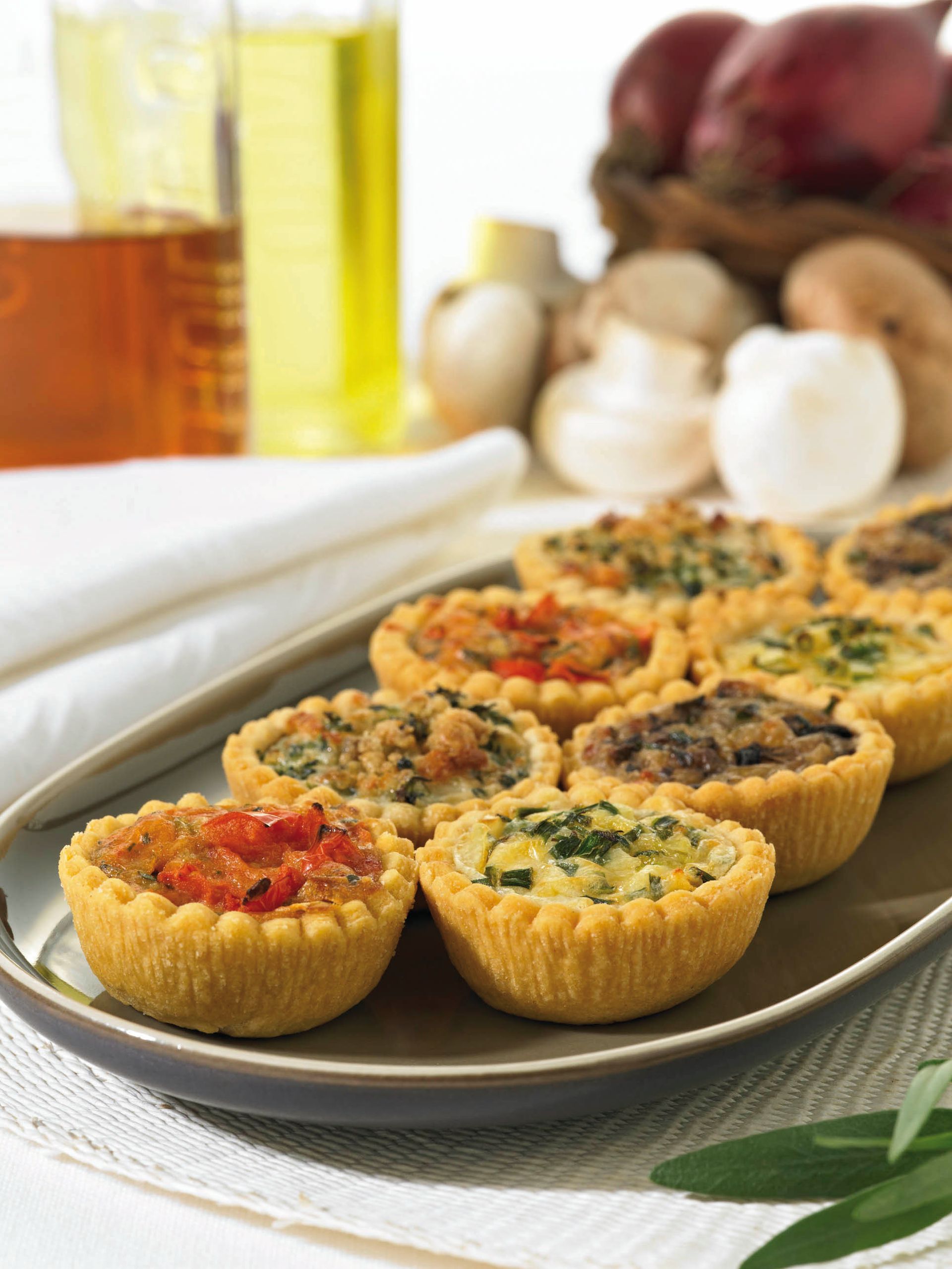Assorted mini savory tartlets on a plate, with olive oil and garlic in the background.