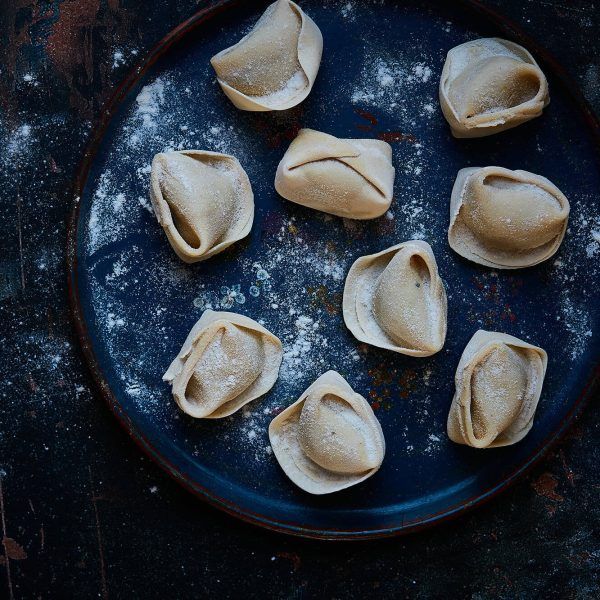 Eight small dumplings on a dark blue plate dusted with flour.