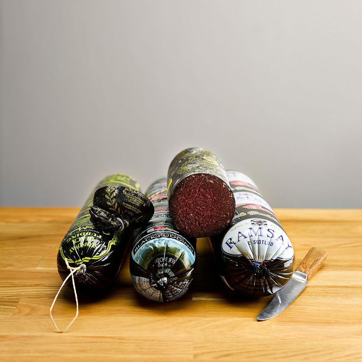 Three colorful decorative rolled candles with twine on a wooden table against a plain wall.