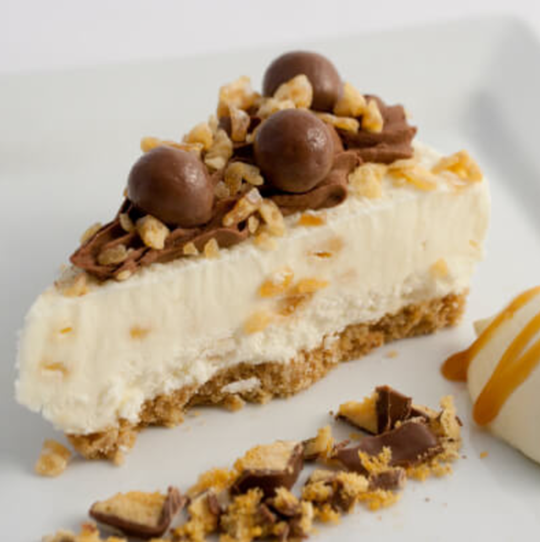 Slice of cheesecake topped with chocolate balls, nuts, and crumbs on a white plate