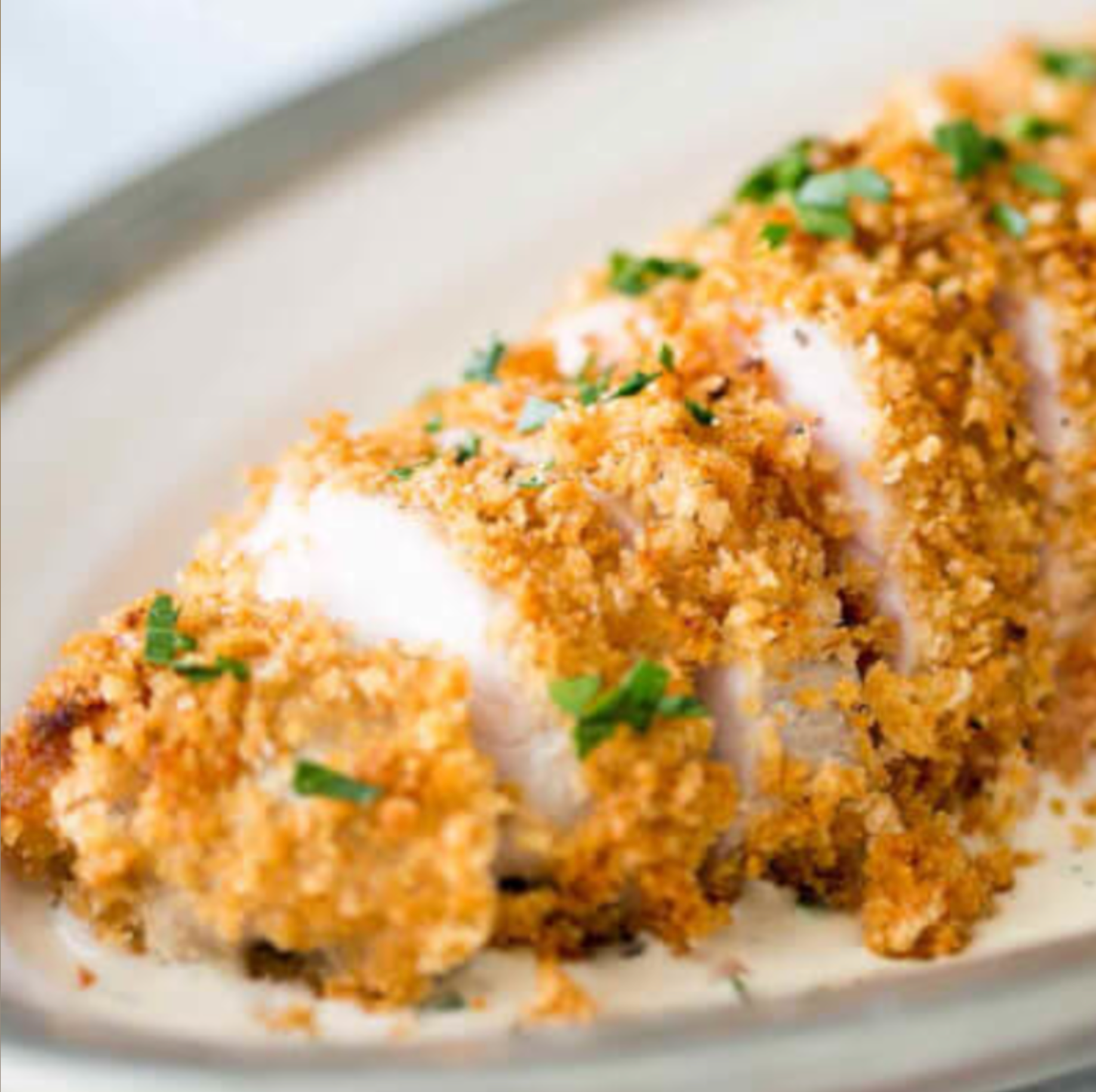 Breaded sushi roll sliced on a white plate, topped with green herbs and a creamy sauce drizzle