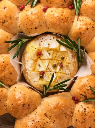 Rustic bread bowl with creamy soup, croutons, knife, and festive pinecones on a dark table.