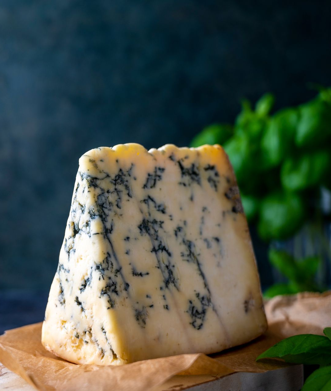 Blue-veined cheese wedge on parchment with blurred green leaves in the background
