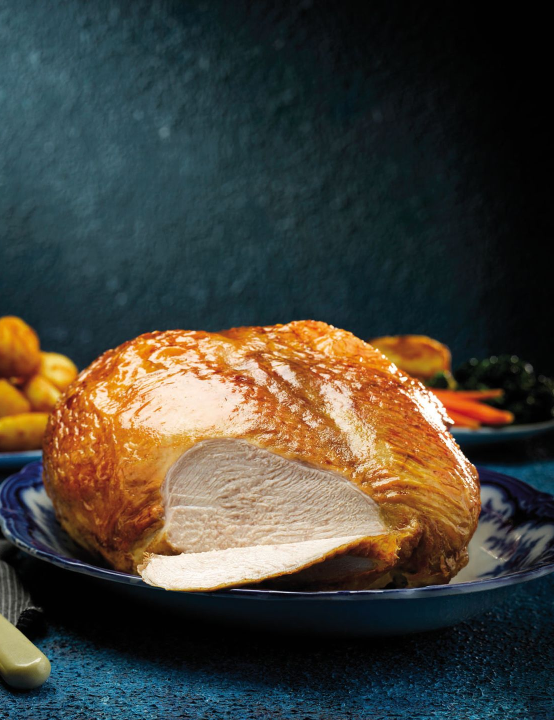 Roasted turkey on a dark plate with potatoes and a knife on a blue tablecloth