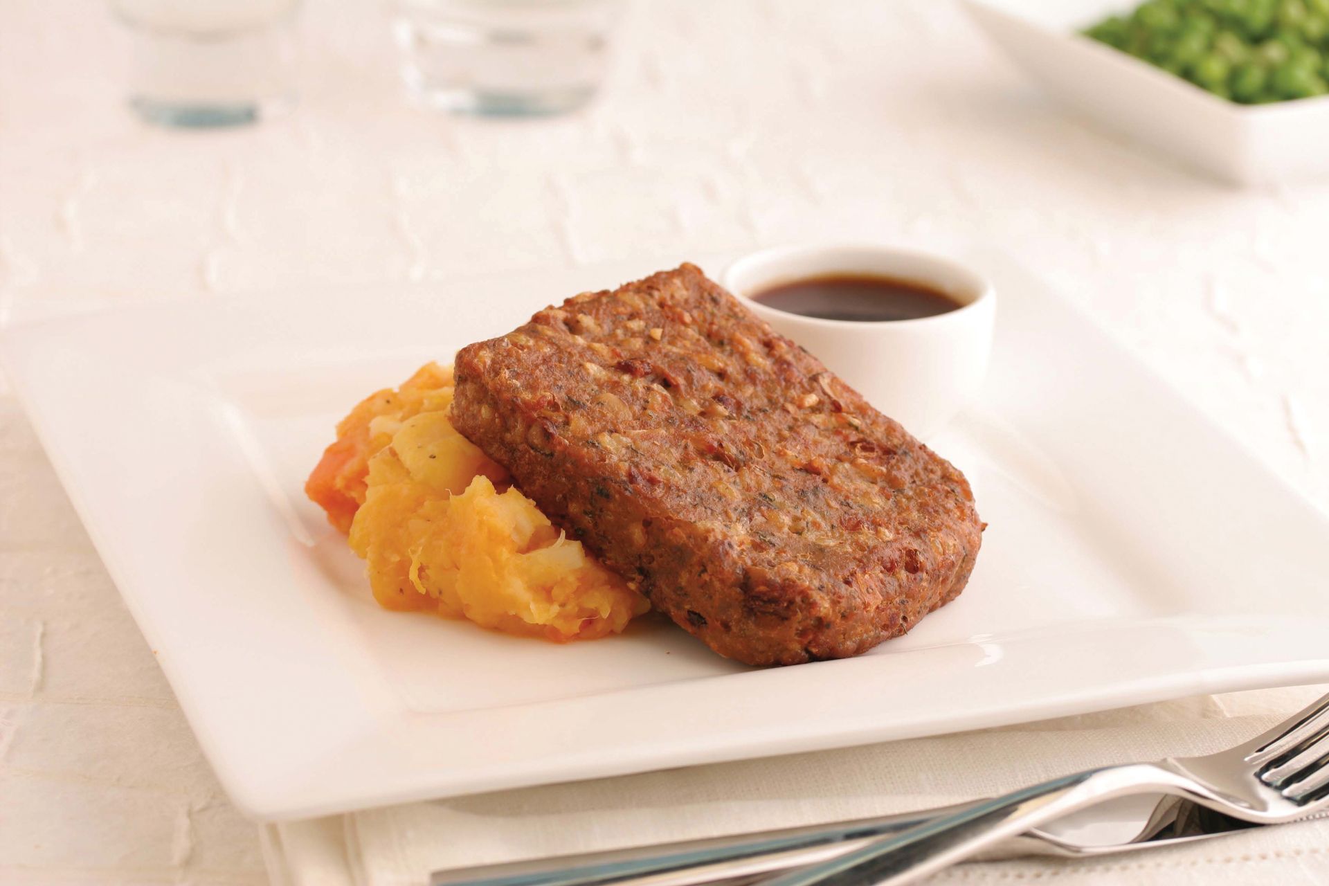 Steak with mashed potatoes on a white plate, with a small cup of sauce on a white tablecloth.