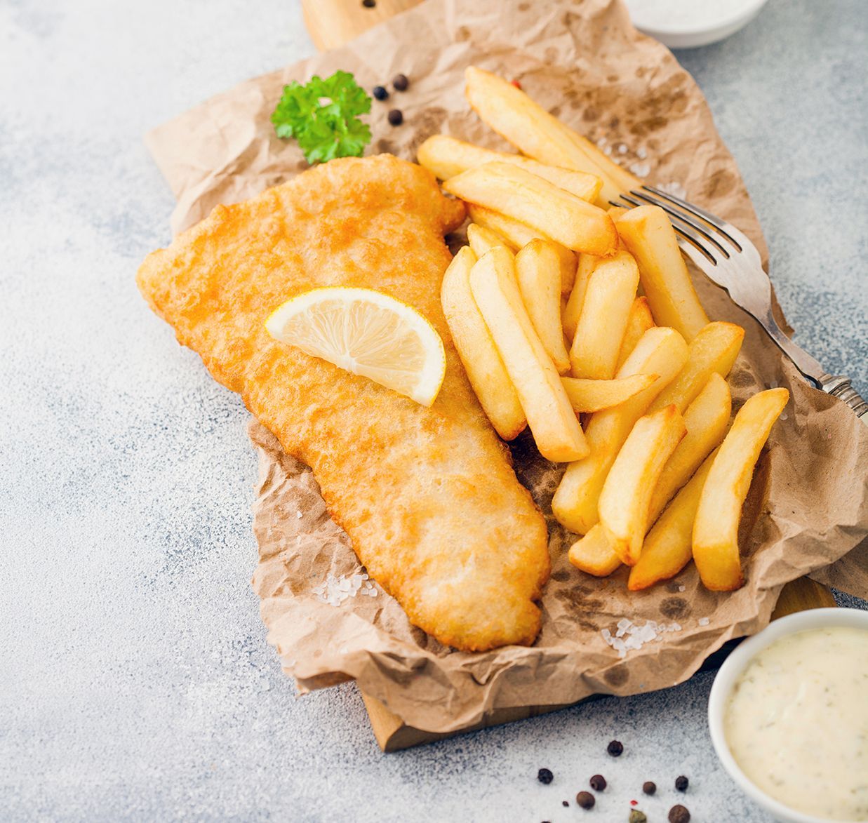 Fish and chips with lemon on brown paper, served with tartar sauce