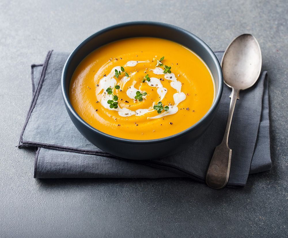 Black bowl of creamy orange soup garnished with herbs and cream on a folded napkin, spoon beside it