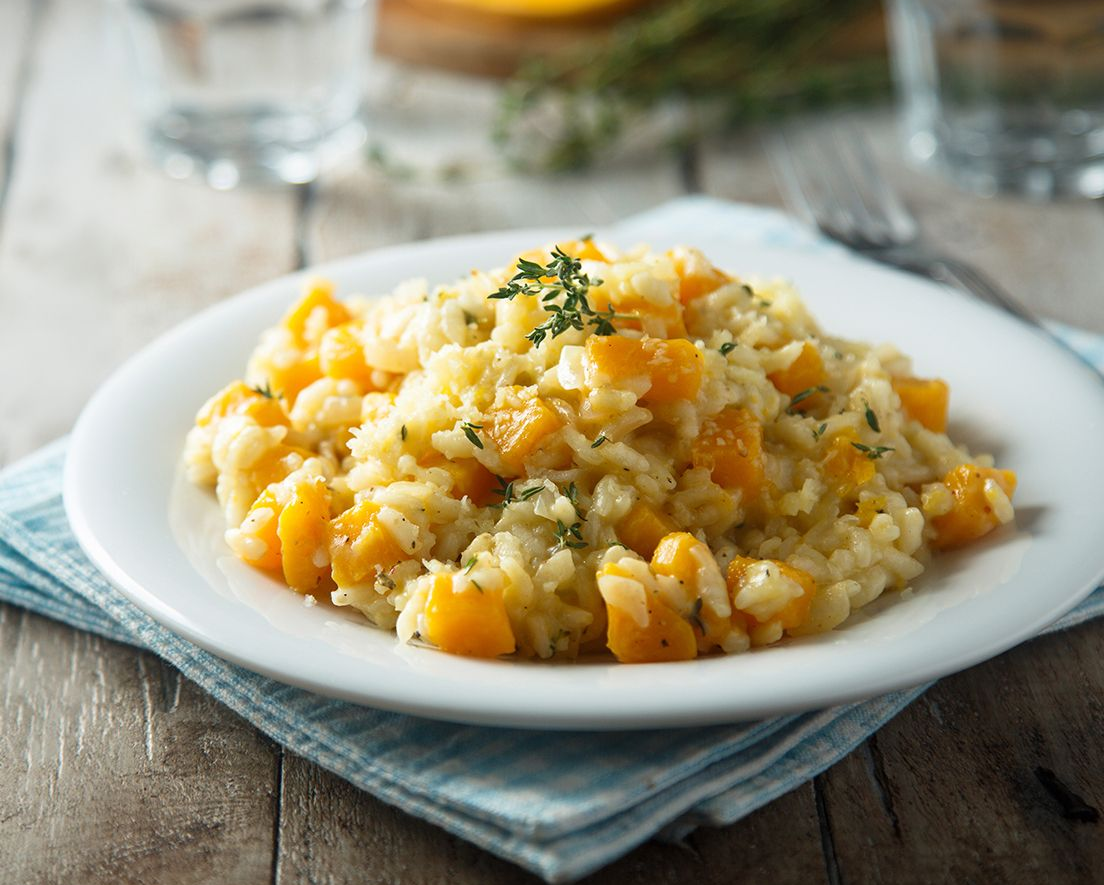 Plate of creamy risotto with orange squash and herbs on a white dish