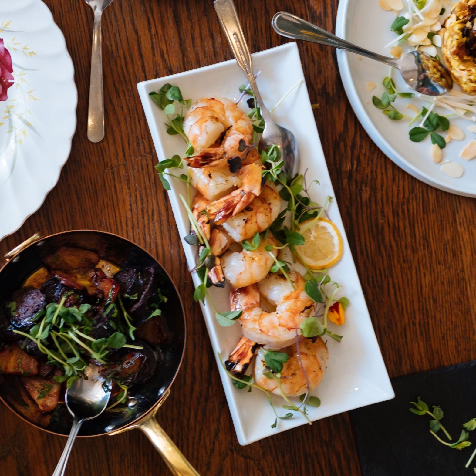 Overhead view of a seafood spread with shrimp skewers, a bowl of mussels, and plated dishes on a wooden table