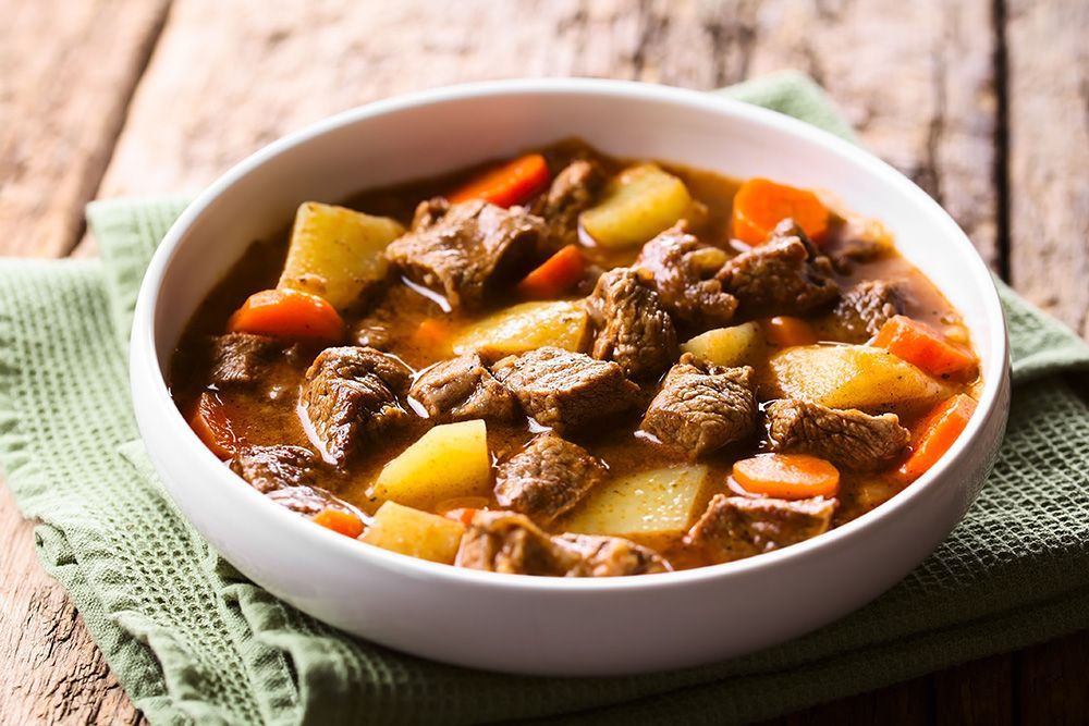 Bowl of beef and vegetable stew on a rustic wooden table with a green cloth napkin