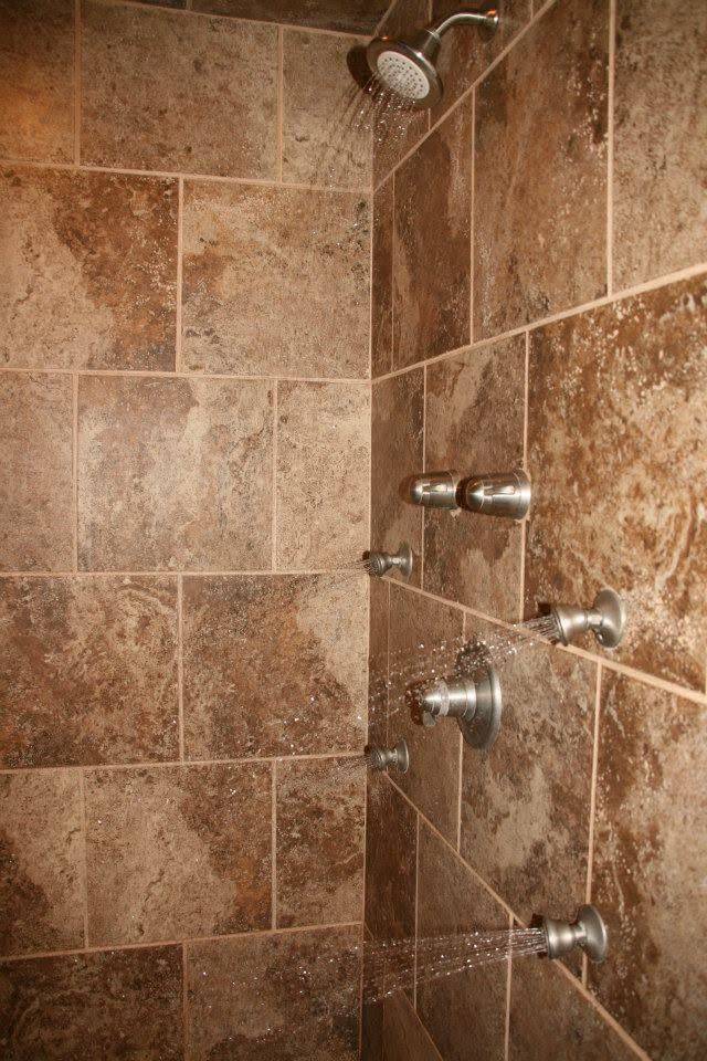 Tiled shower with multiple chrome body spray nozzles and a showerhead.