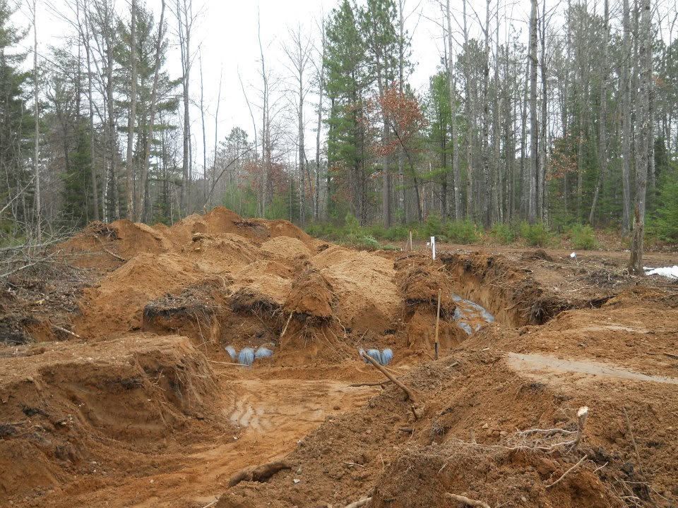 Large muddy excavation pit in a forest clearing with exposed earth and trees in the background