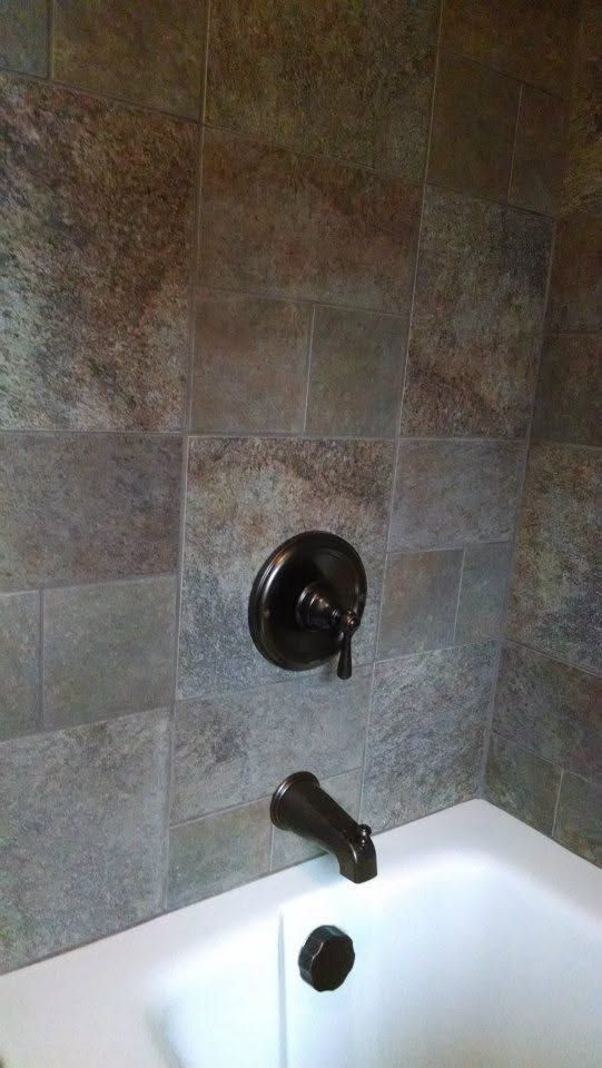 Bathroom wall with tiled shower surround, dark shower fixture, and white tub rim.