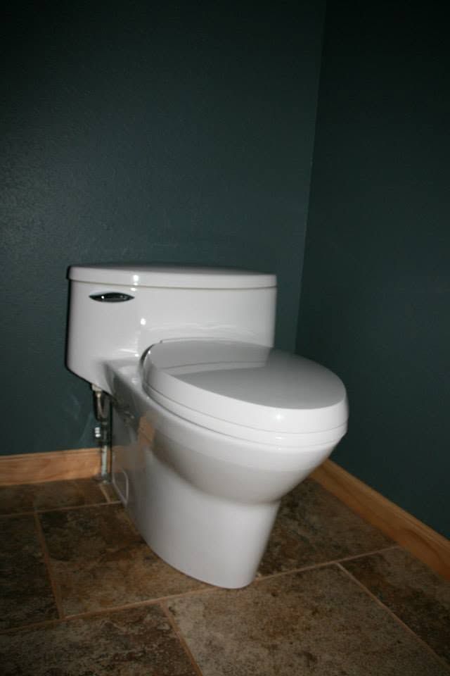 White toilet in a small bathroom with dark green walls and brown tile floor