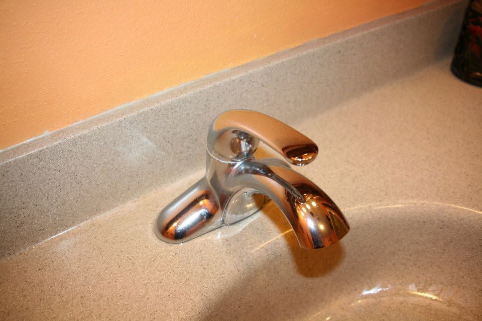 Chrome bathroom faucet on a beige sink with an orange wall behind it