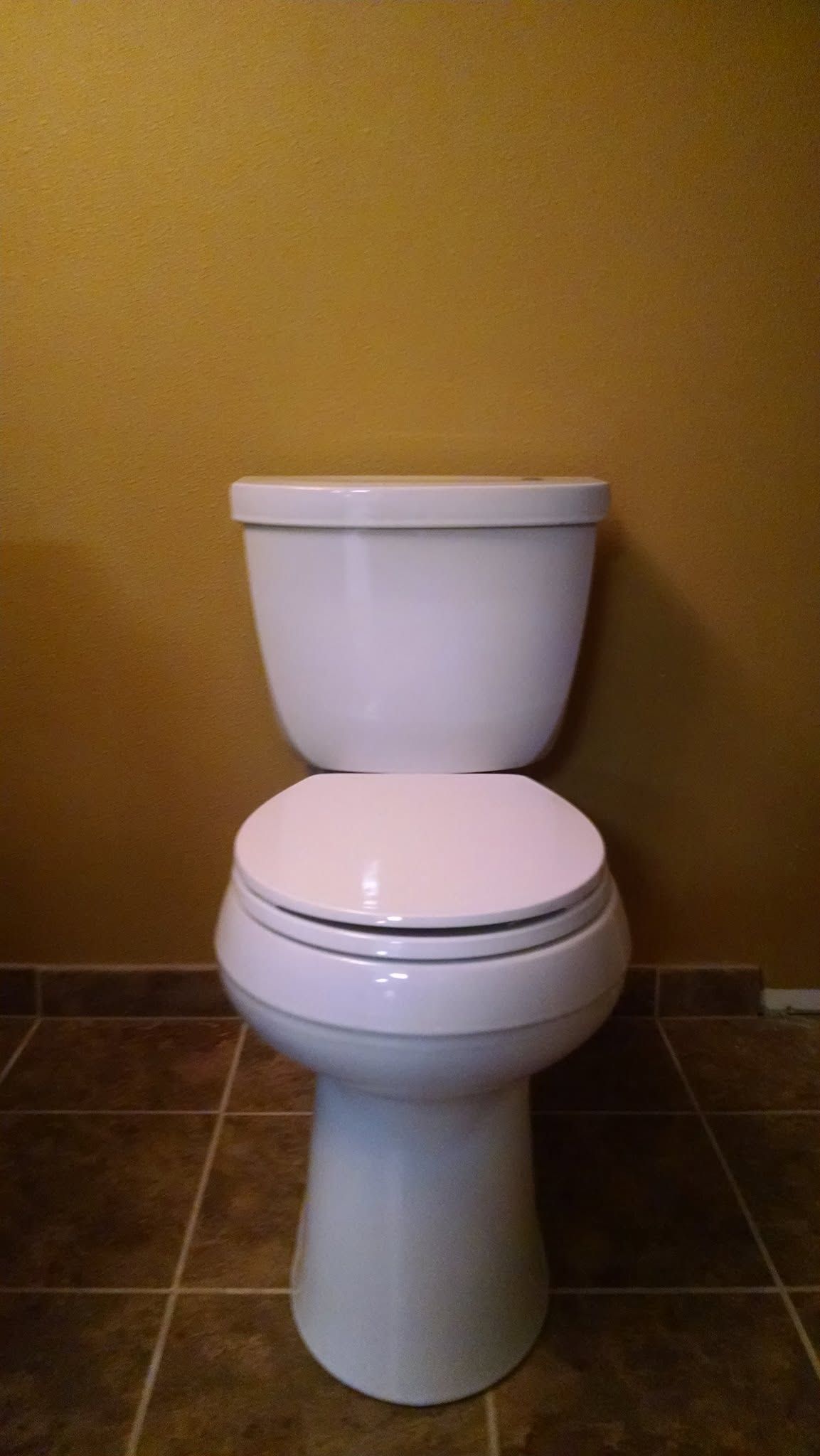 White toilet with closed lid against a tan wall in a tiled bathroom.