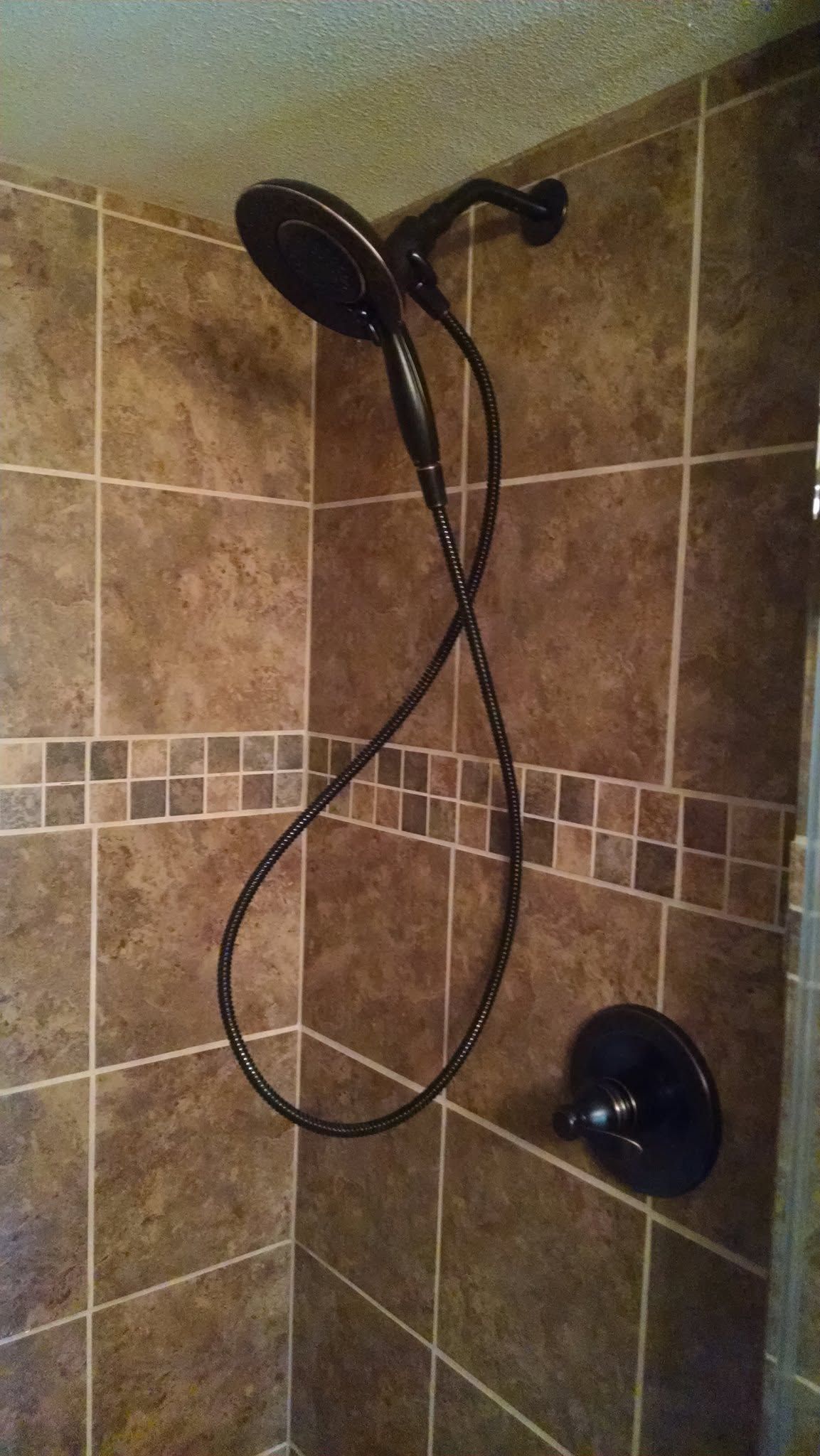 Corner shower with tiled brown walls, handheld showerhead, and wall-mounted shower control.