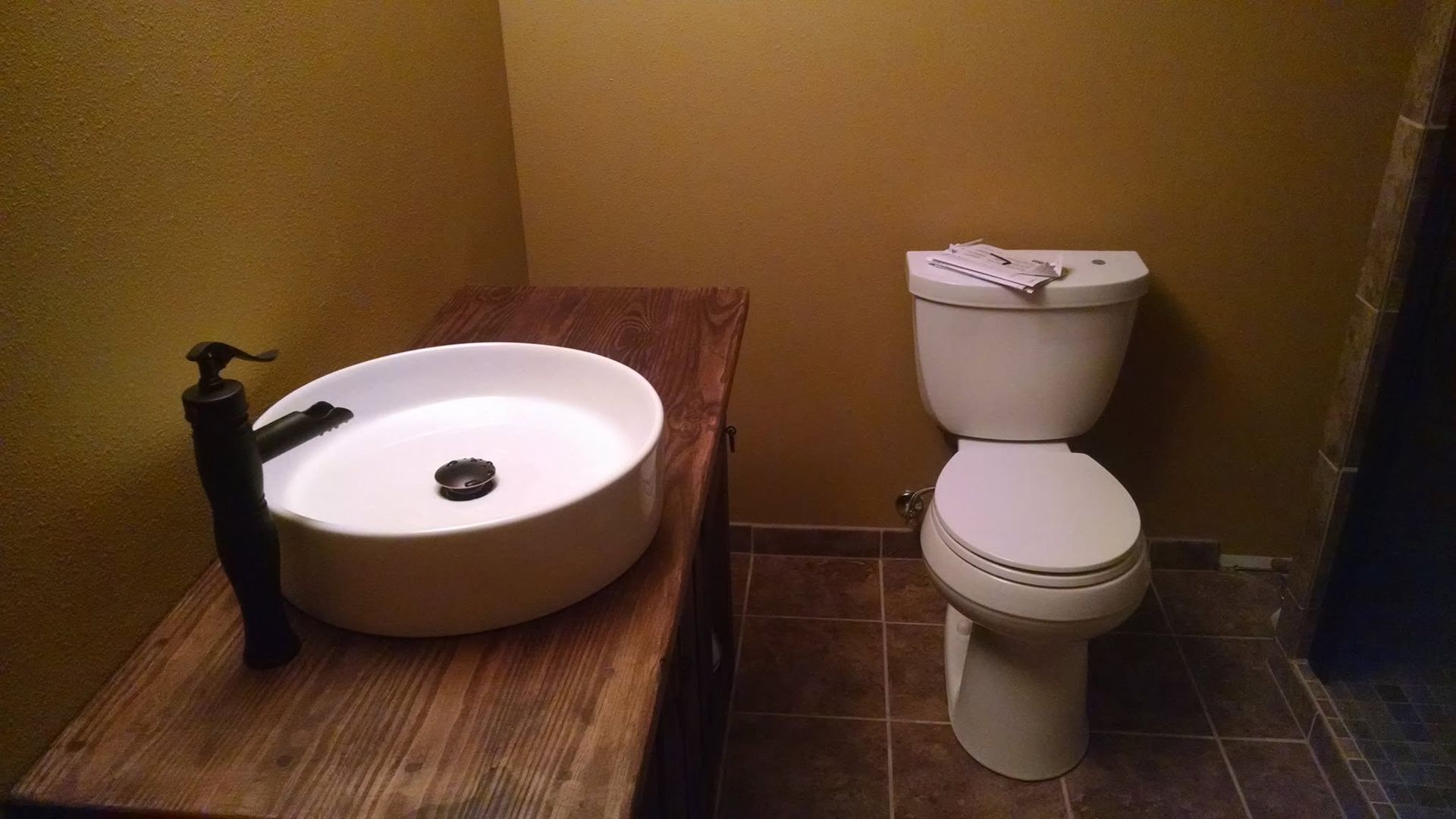 Small bathroom with a round sink on a wooden counter and a white toilet against yellow walls.