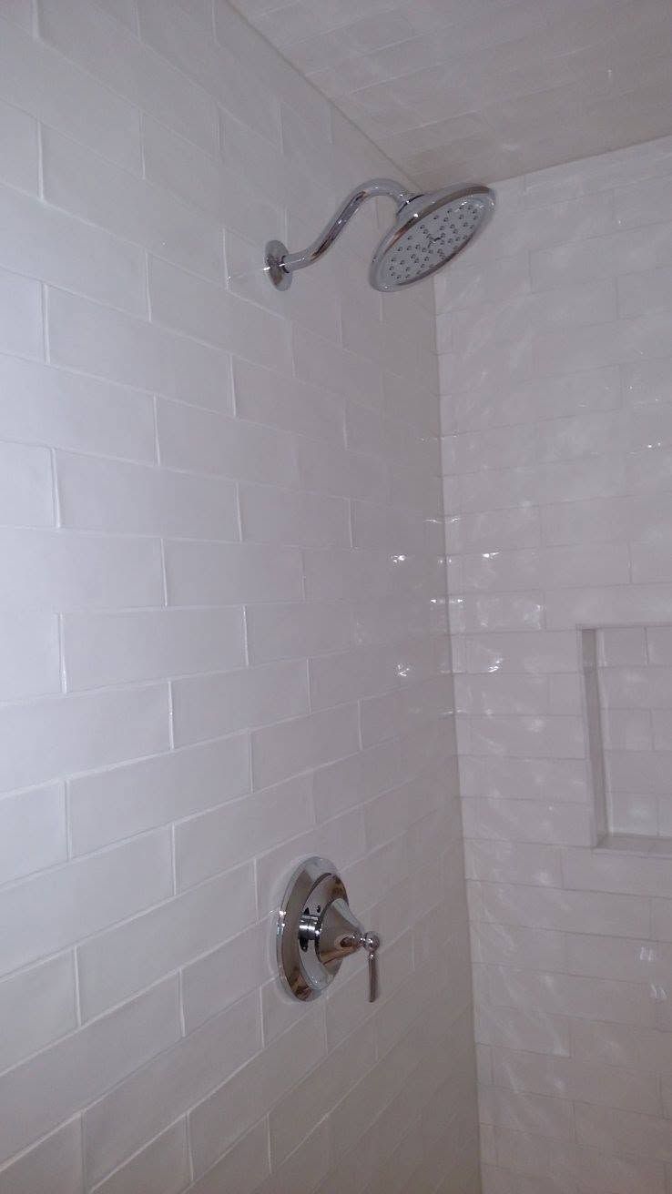 White tiled shower with chrome showerhead and faucet on a light-colored wall.