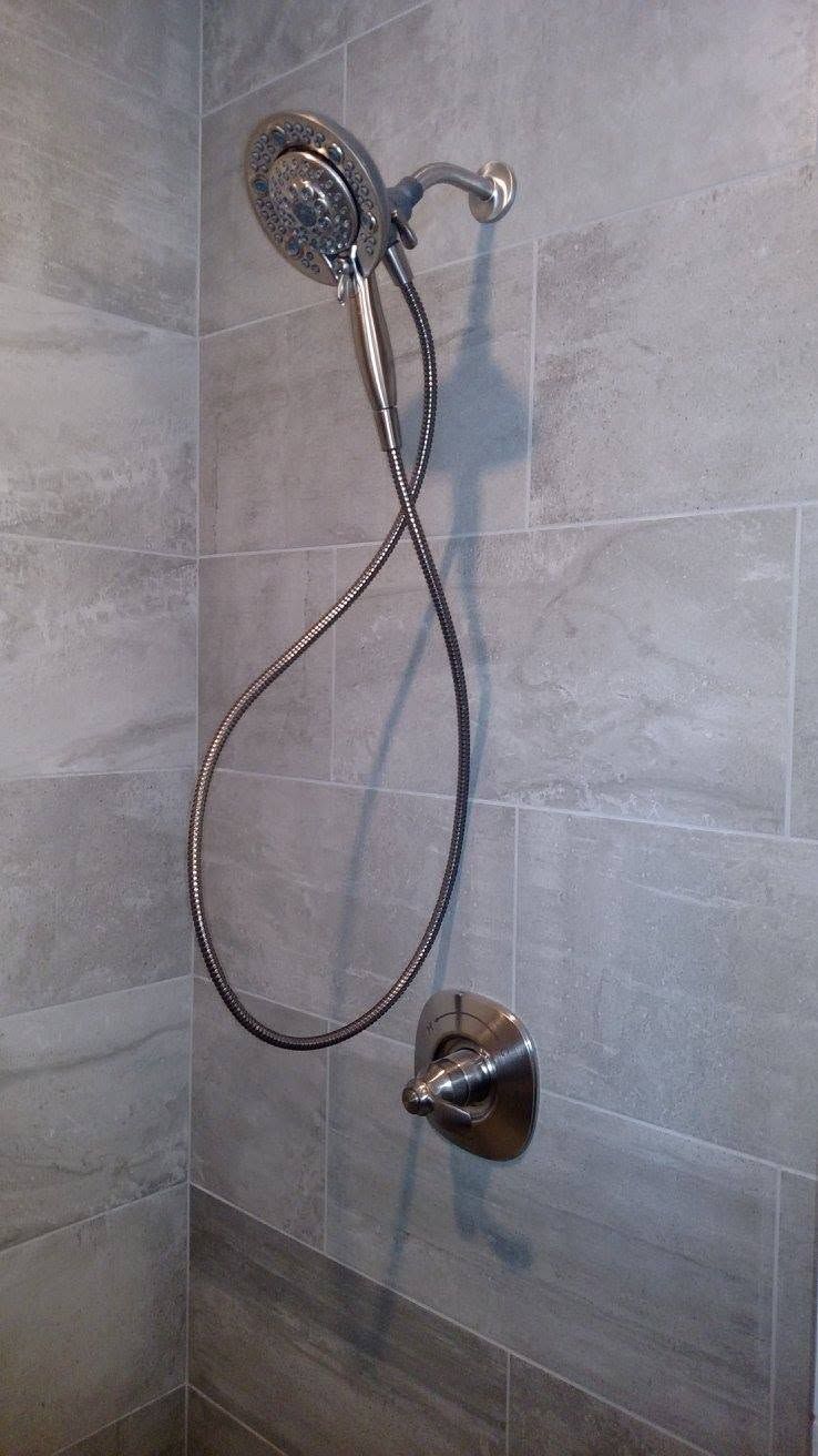 Chrome showerhead and handheld shower hose with faucet on gray tiled bathroom wall