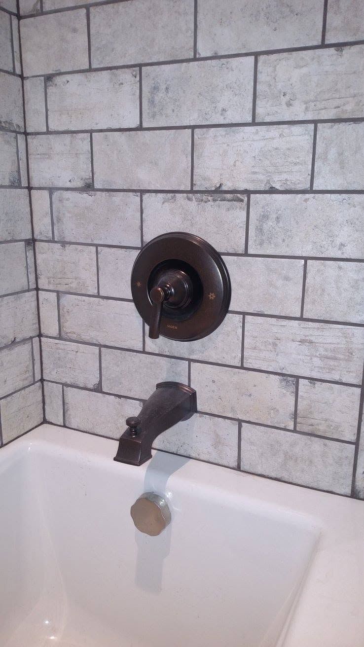 Bathroom tub faucet and wall-mounted shower control on gray tiled wall