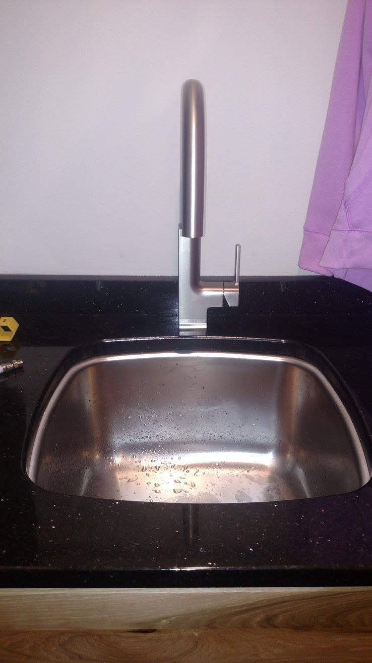 Kitchen sink with stainless steel basin, black countertop, and tall chrome faucet.