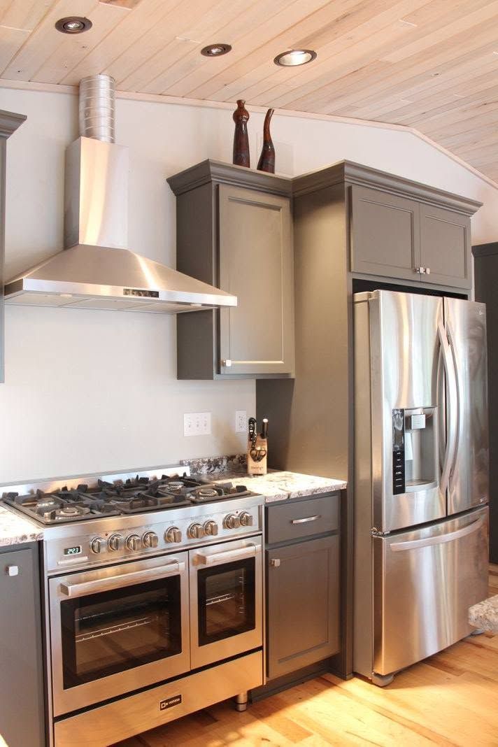 Modern kitchen with stainless steel stove, refrigerator, and range hood under wood-paneled ceiling