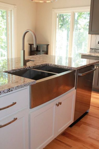 Bright kitchen island with black countertop, white cabinets, granite sink, and sunlight from large windows