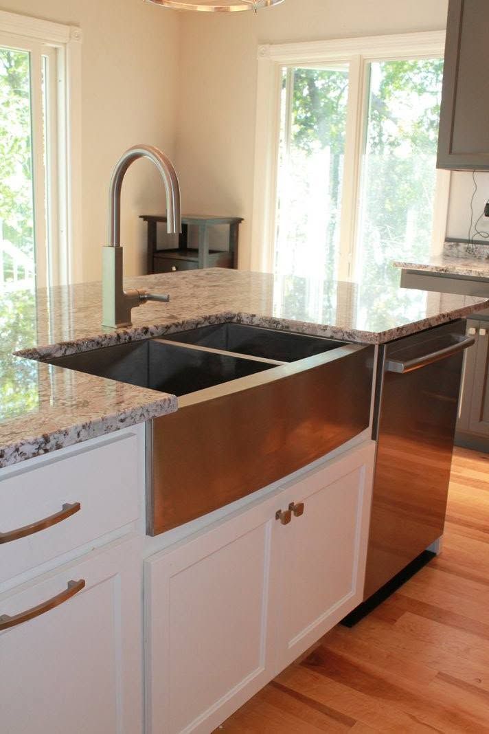 Kitchen island with double sink, wood base, granite countertop, and stainless dishwasher in a bright kitchen