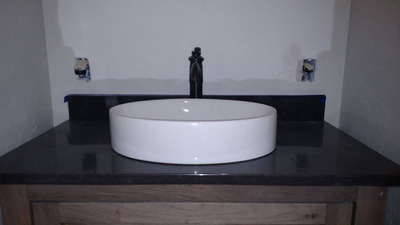 Modern bathroom sink with round white basin on a dark countertop and black faucet.