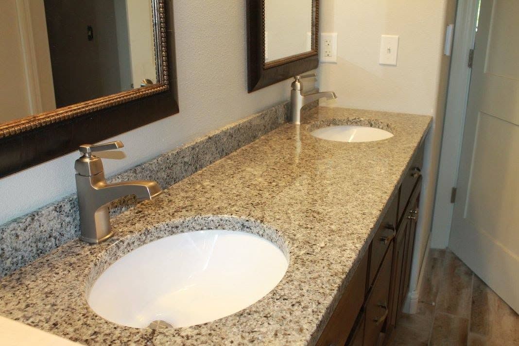 Bathroom vanity with double sinks, granite countertop, mirrors, and wood floor
