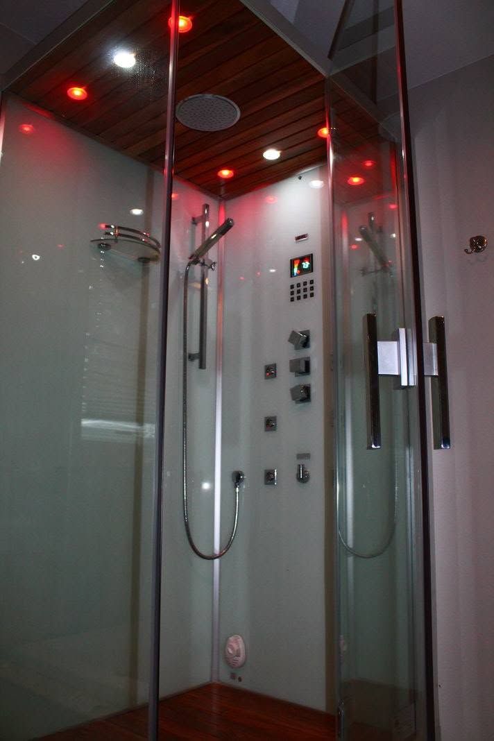 Glass shower stall with chrome fixtures, control panel, and red ceiling lights